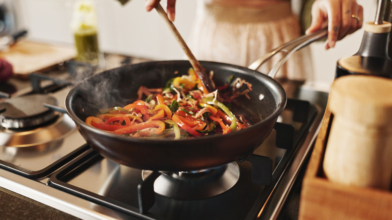 Close up of person sauteing peppers in black pan