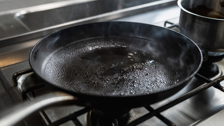 Shallow black pan on stove stop steaming with some oil