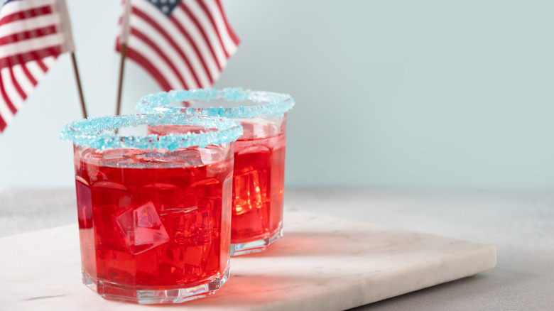 Two red cocktails with blue sugar rims pictured with two small American flags.