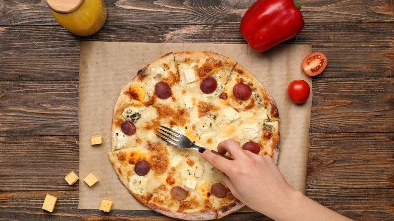 Hand with fork poking a pizza on wooden background