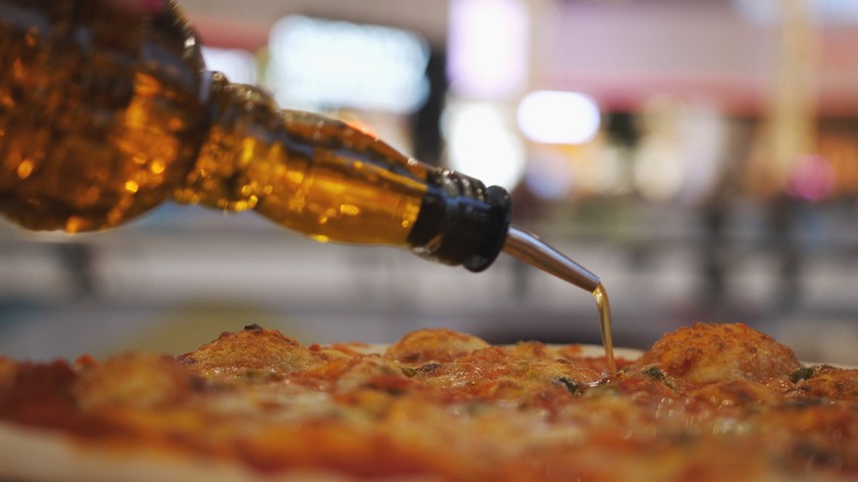 Close-up shot of oil being poured onto an already baked pizza with blurred lights in the background.