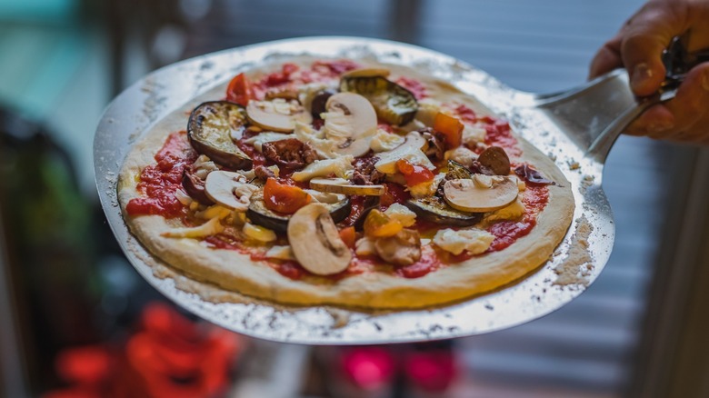 Uncooked pizza on a round metal pizza peel
