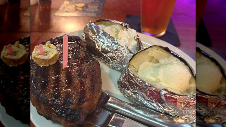 A buttered steak on a restaurant plate next to potatoes wrapped in foil.