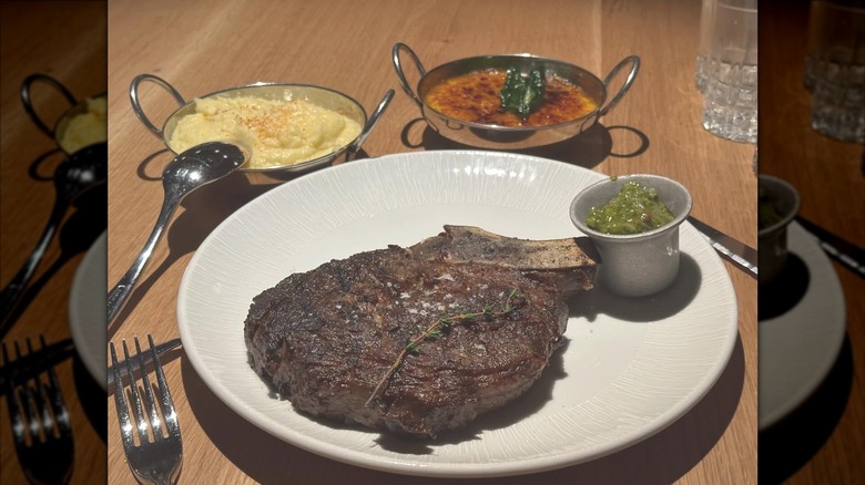 A steak plate resting on a wooden table next to sauces in silver tureens.