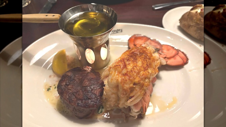Steak, a lobster tail, and melted butter arranged on a plate.