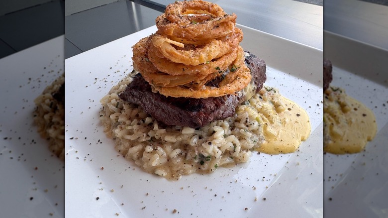 Steak rests on a bed of creamy rice and topped with onion rings on a white plate