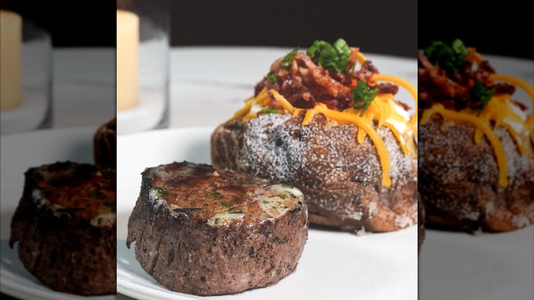 A buttery steak and a baked potato arranged on a white restaurant plate.