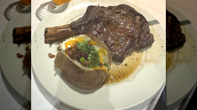 Bone-in steak and a baked potato with chives on a plate.