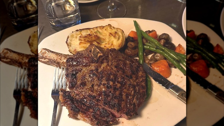 A restaurant plate heaped with bone-in steak, a baked potato, and vegetables.