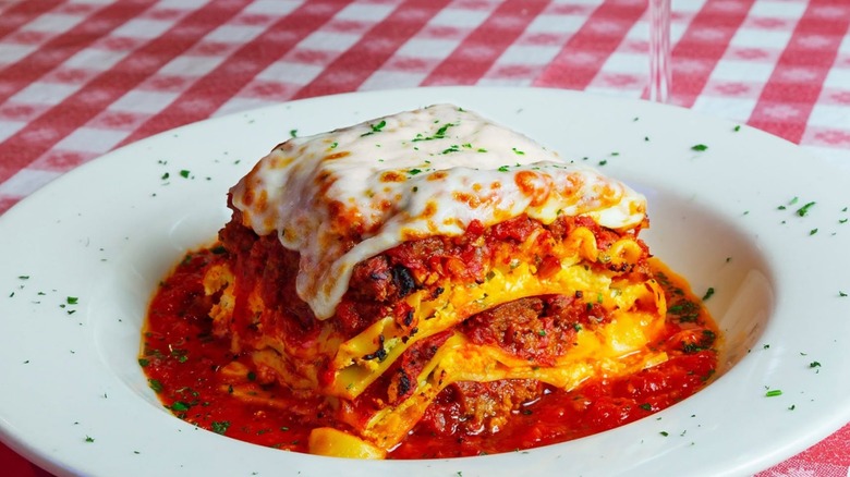 Serving of Buca di Beppo Lasagna on a white plate on a table with a red and white checkered tablecloth