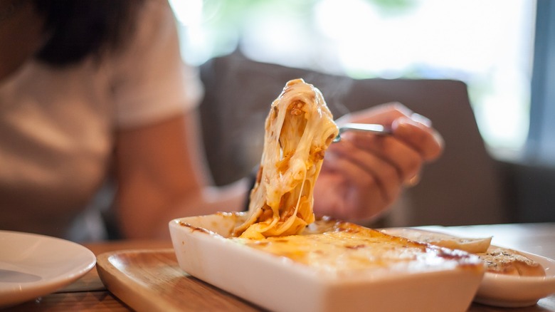 Person eating a big forkful of lasagna in a white casserole dish