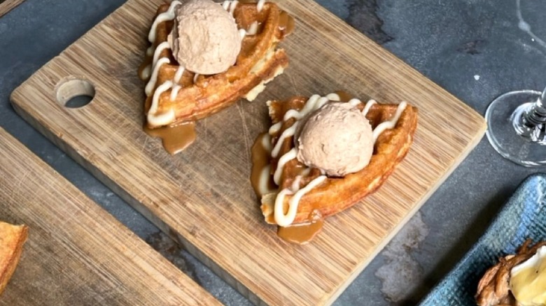 Two slices of Cafe Tu Tu Tango waffle with icing drizzle and scoop of ice cream on wooden board