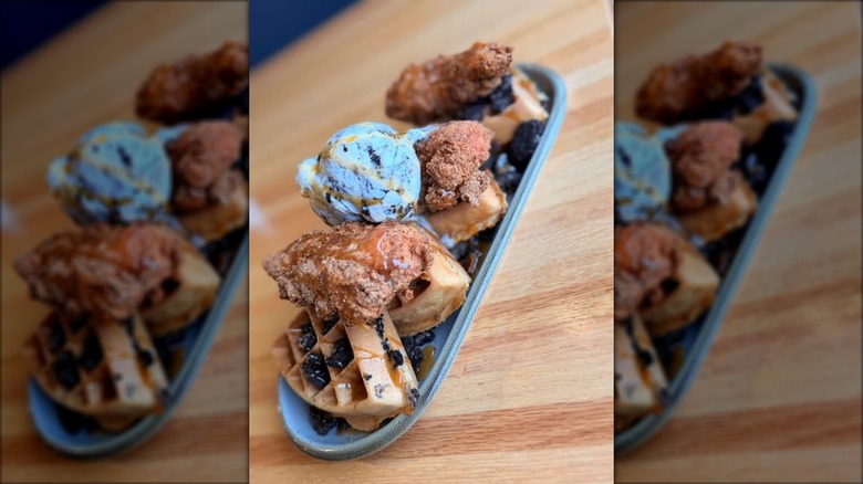 Belgian waffle on plate topped with fried chicken, oreo crumbles, and scoop of ice cream