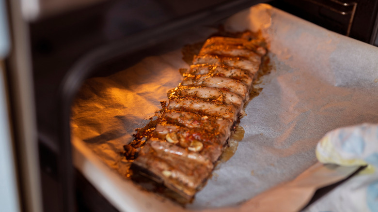 Person taking pork ribs out of the oven