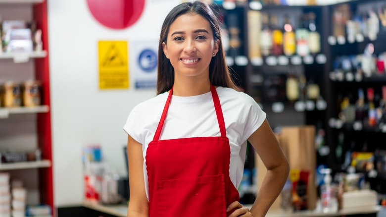 A female grocery store worker wearing a red apron