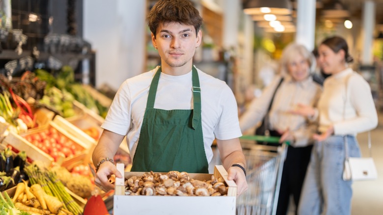 Guy store employee carries box of mushrooms into sales area