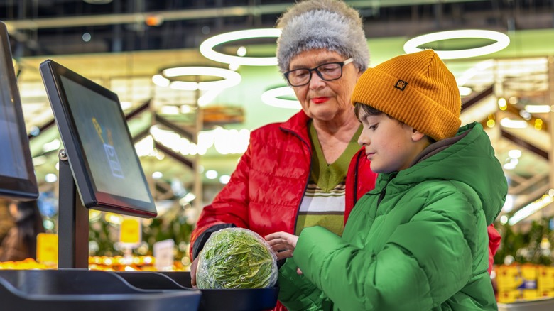 Young boy using self-checkout scale with grandmother