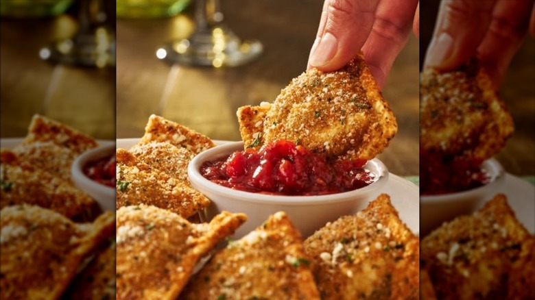 A hand dipping an Olive Garden toasted ravioli in a sauce, mirrored
