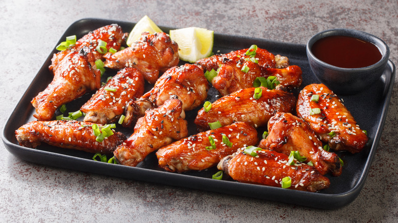 asian wings on black platter with extra sauce in black ramekin