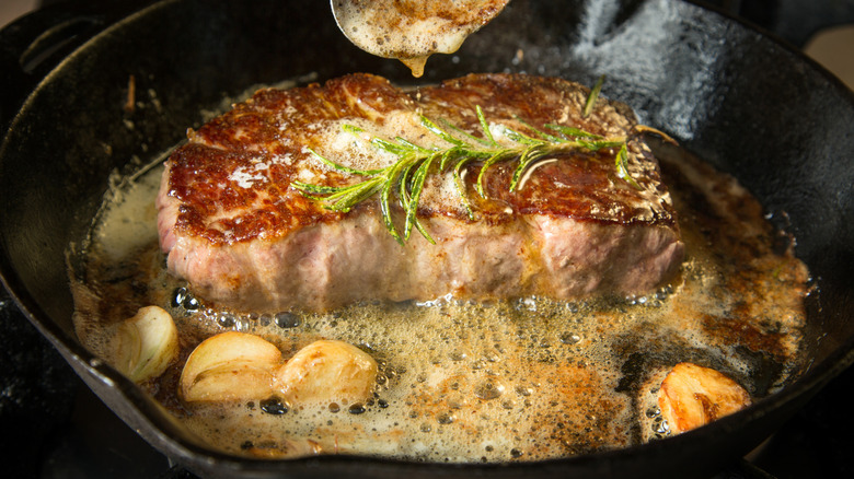 seared steak cooking in melted butter with garlic cloves