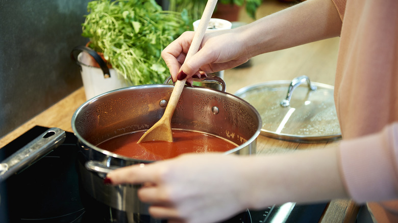 Women's hands stirring a red sauce in a pot