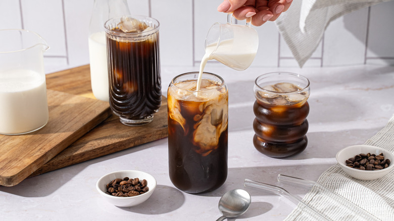 A glass of iced coffee with creamer being poured into it