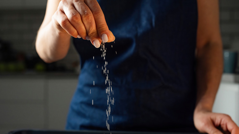 Person's hand sprinkling a pinch of salt