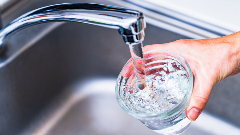 A chrome kitchen tap pours water into a glass that a person's hand is holding