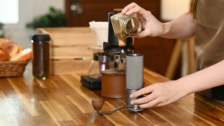 A woman pouring coffee beans into a grinder on a wooden table