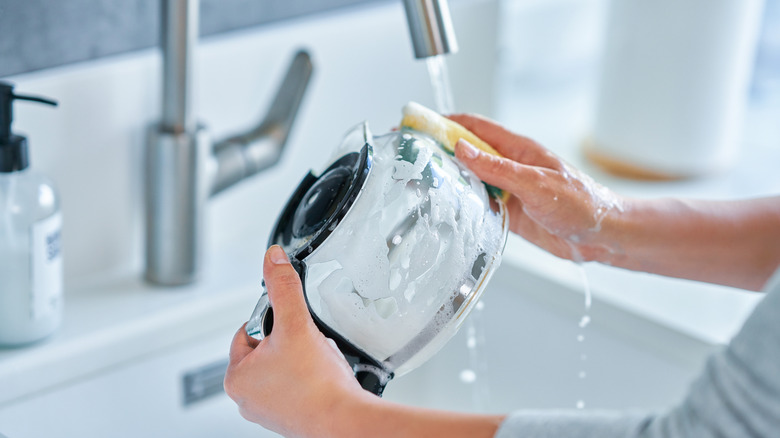 A coffee pot being scrubbed with a sponge in the sink
