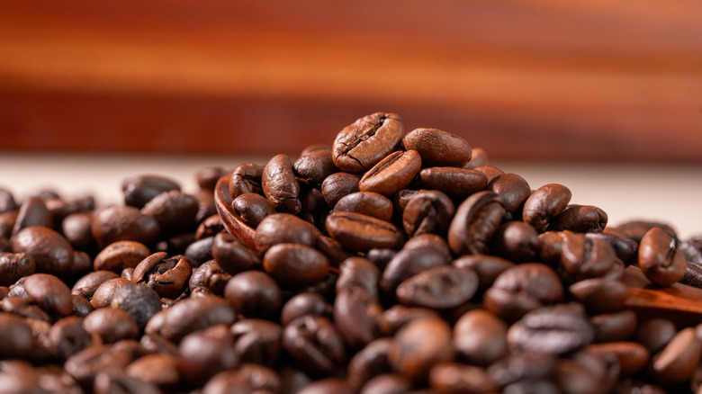 A closeup of a mound of coffee beans on a white table with a brown and orange background