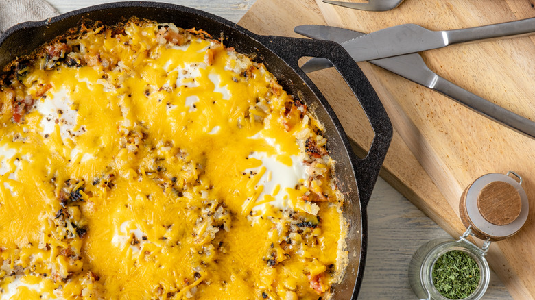 Hash browns with egg and sausage topped with cheese in a skillet