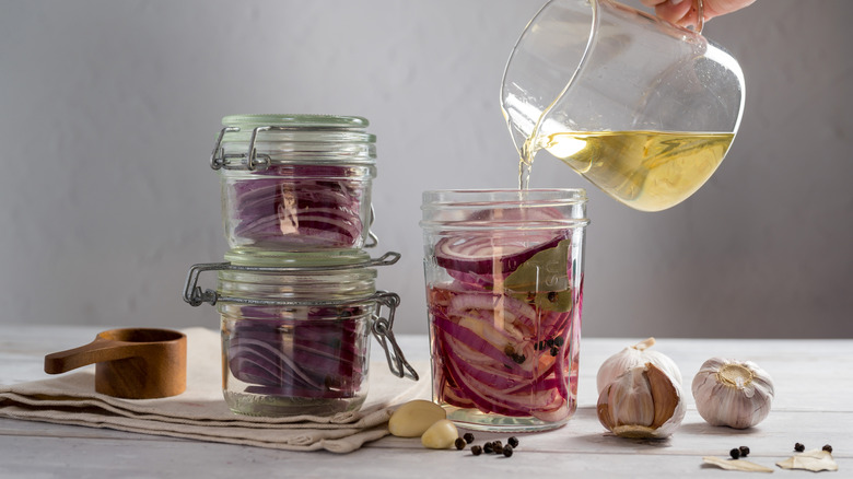 Homemade pickled red onions in jars with a jug of vinegar being poured in