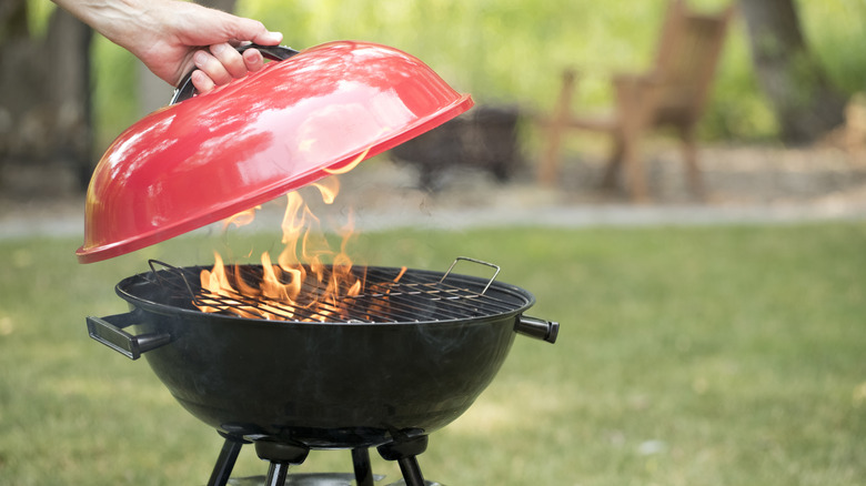 A red grill with the lid being lifted, in a garden