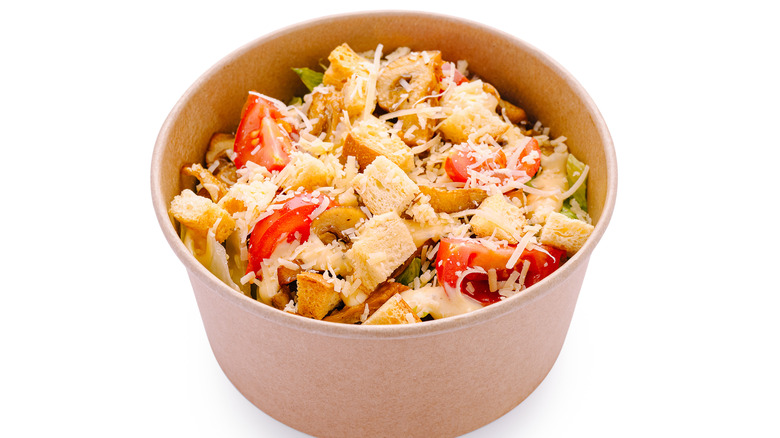 A bowl of salad greens topped with pieces of chicken, diced tomatoes, and croutons