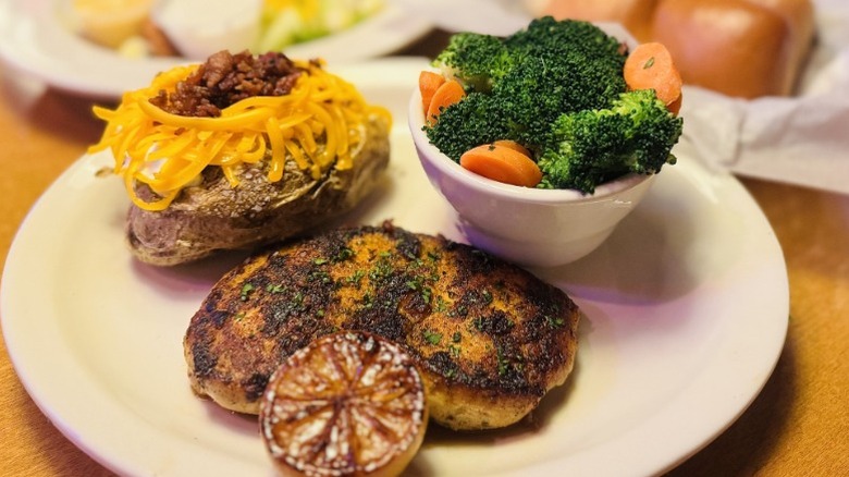 Texas Roadhouse herb-crusted chicken, cheese-topped baked potato, and broccoli with carrots on a white plate