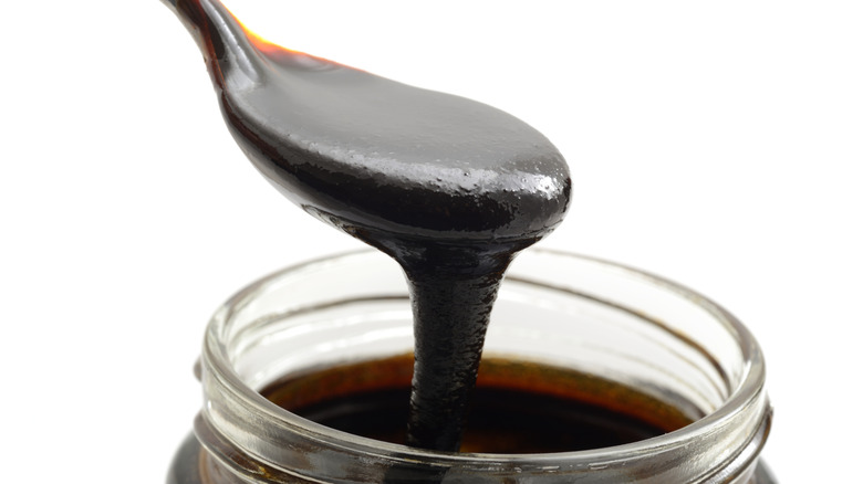 Organic Molasses being scooped out of a jar, shot against a white background.