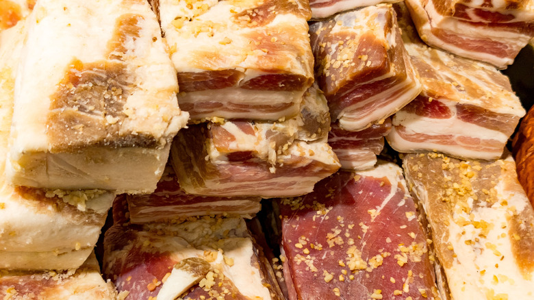 Close-up view of thick cuts of cured pork belly, showing layers of fat and meat. The pieces are generously coated with garlic and spices, highlighting the texture and marbling