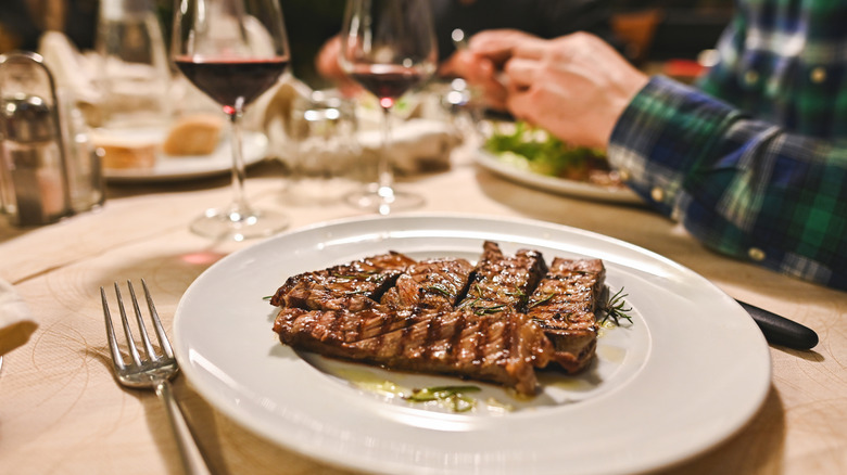 Plate with steak next to glass of wine on table