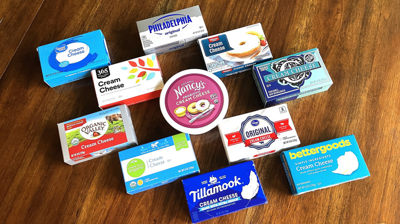 an array of 11 different brands of cream cheese are laid out geometrically on a dark wood table