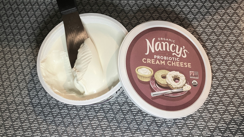 a knife scoops into a tub of Nancy's Probiotic thick cream cheese with the lid leaning against the side