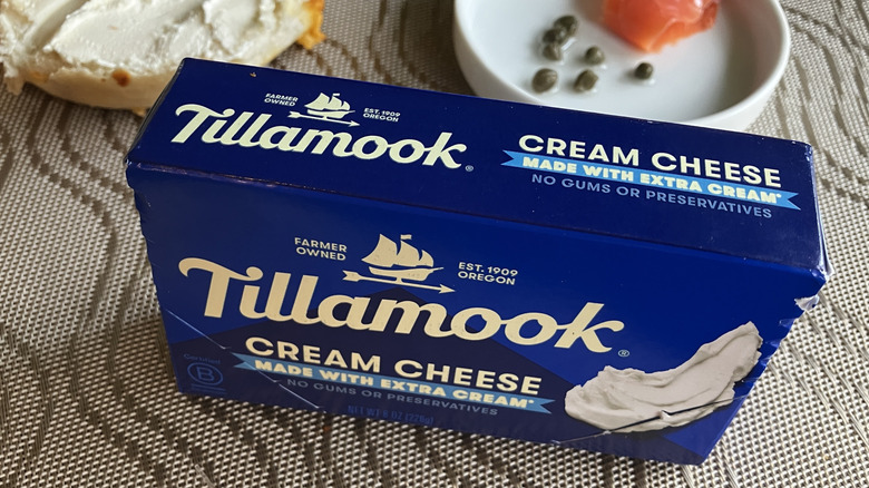 a blue box of Tillamook cream cheese set on its side with bagel and toppings in the background