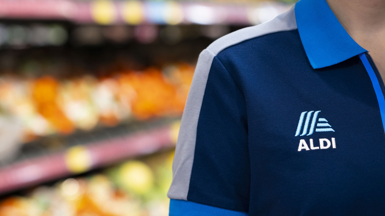 Close-up of a person wearing an Aldi shirt, the produce aisle blurred in the background