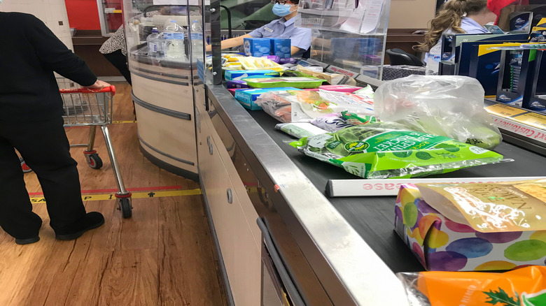 A uniformed cashier wearing a mask and sitting behind the cash register at a grocery store