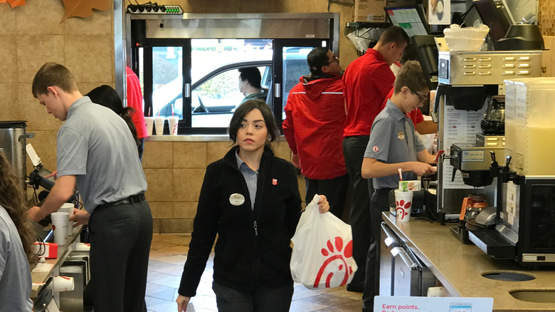 Chick-fil-A workers behind the counter, with a manager walking and holding a bag