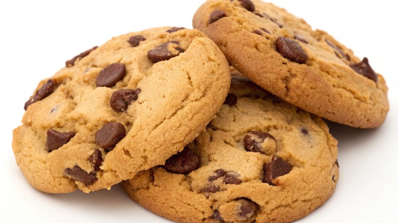 Three chocolate chip cookies are stacked on a white background