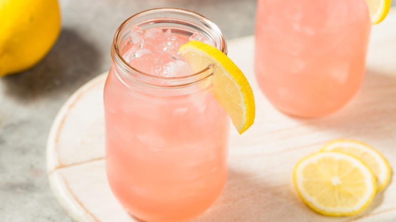 Iced pink lemonade drink in a glass jar with ice cubes and lemon slices