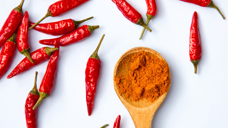 Cayenne pepper in a wooden spoon surrounded by whole peppers