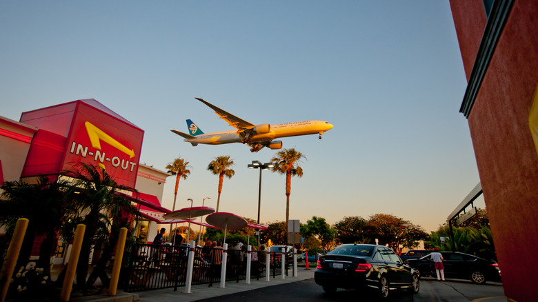 An airplane flies over an In-N-Out location.