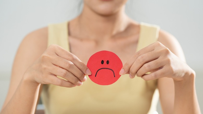 Person holding a red paper circle with a sad face drawn on it